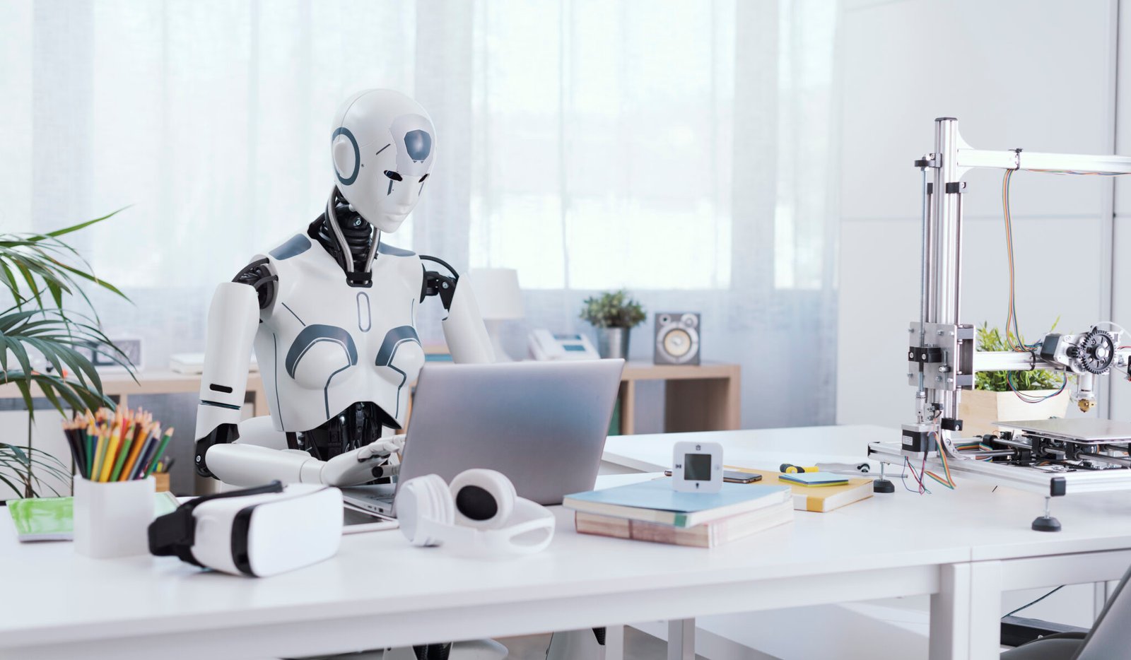 A robot resembling a human sits at a desk in an office, using a laptop to showcase the value of automation in repetitive and menial tasks.